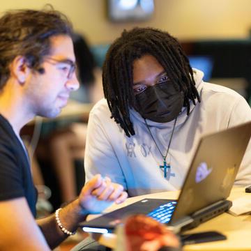 两个学生坐在一张桌子前，在一台开放的笔记本电脑前合作